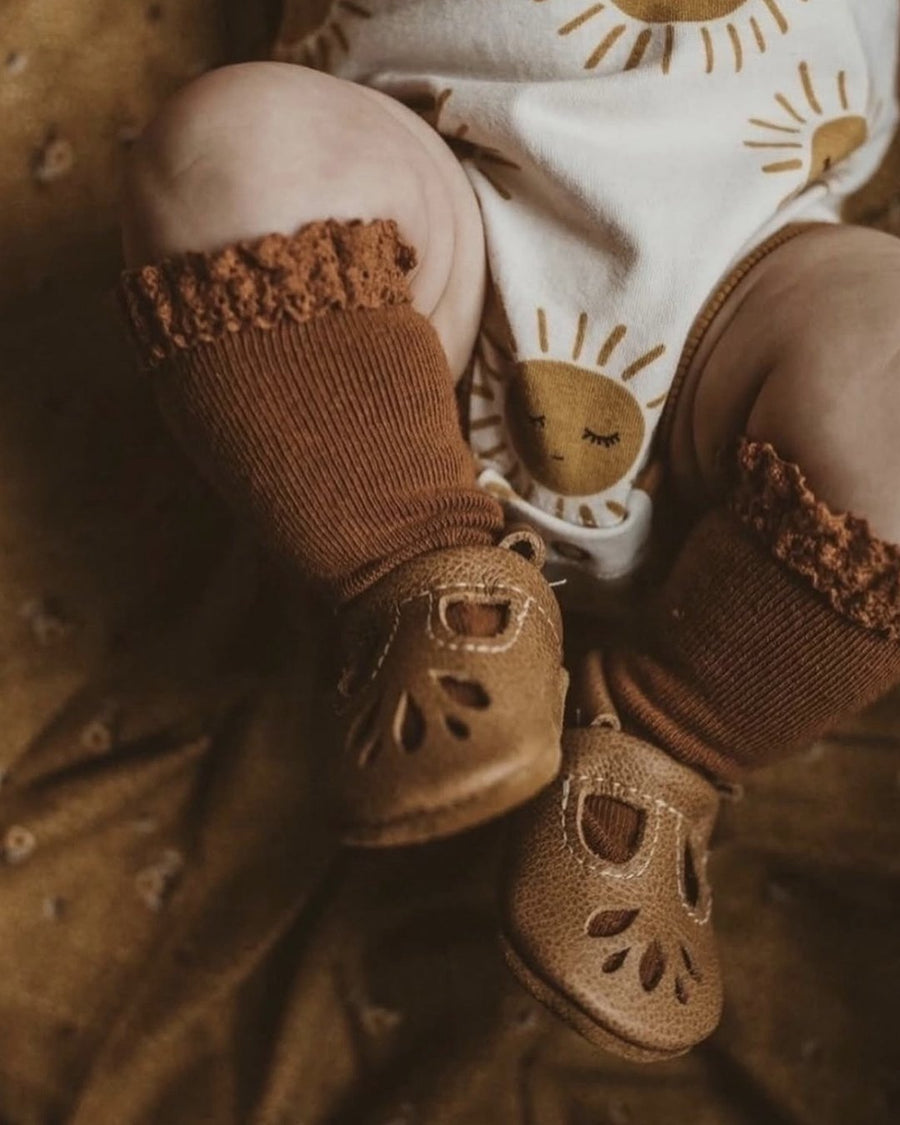Toddler wearing brown leather T-strap shoes with ruffled socks