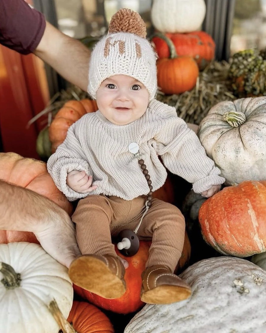 Baby sitting on pumpkins wearing tan leather moccasins
